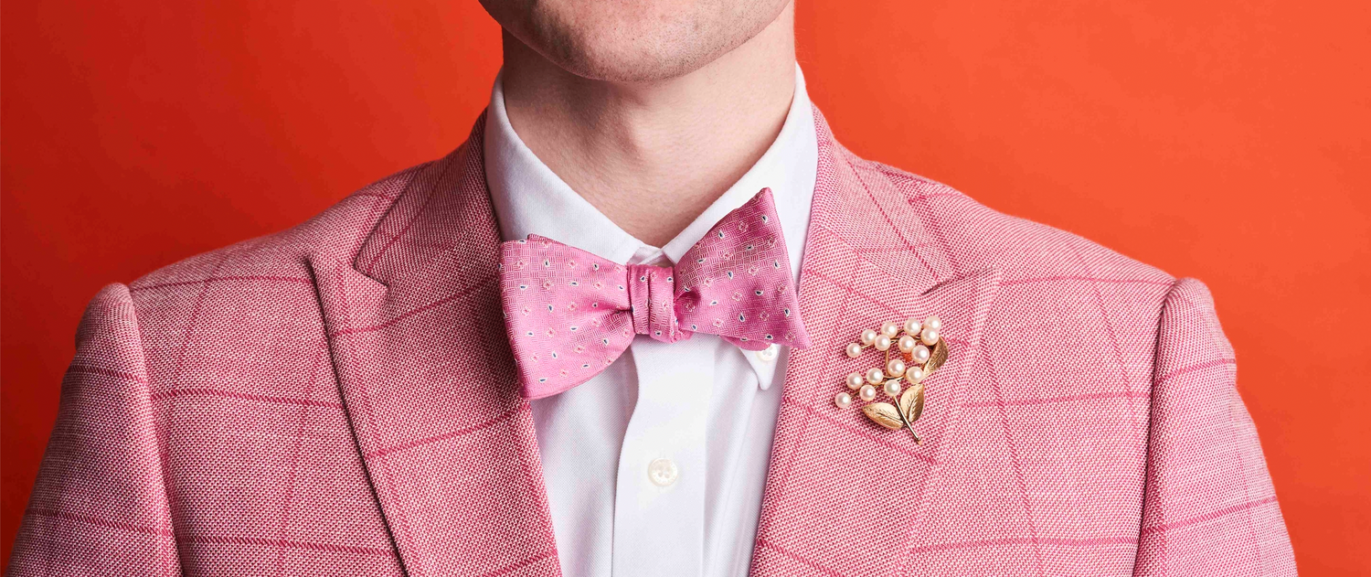 close up of man in pink suit with bowtie wearing a pearl brooche