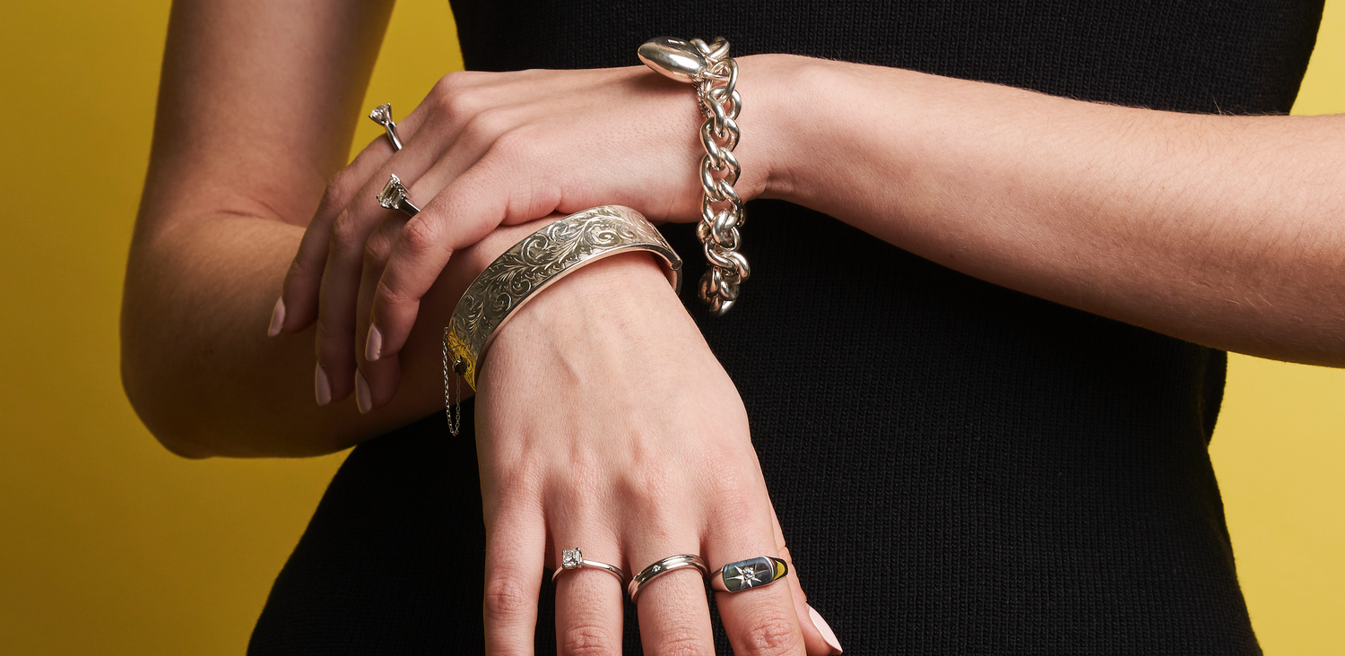 woman posed wearing bracelets and rings on a gold background 